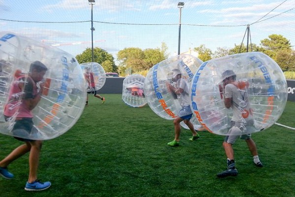 un groupe joue au bubble foot sur le terrain extérieur de l'arena play five de st jory près de toulouse. les personnes sont sur le point de se percuter